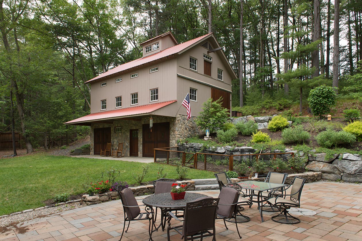 An exterior picture of the Classic Car and Family Recreation Barn, designed and built by Geobarns, with mocha wood siding, copper metal roof, hand-built garage doors, and cupola.