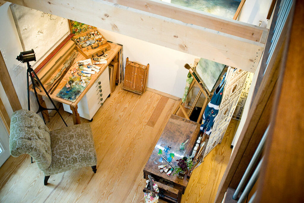 An interior picture of an art studio, designed and built by Geobarns, looking down from a mezzanine catwalk at the artist's painting station.