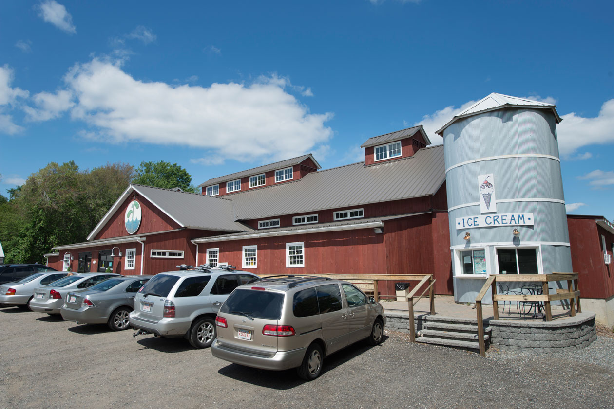An exteriro picture of the Waterfresh Market, design and built by Geobarns, with barn red wood siding, gray metal roof, cupolas, and a silo for selling ice cream.