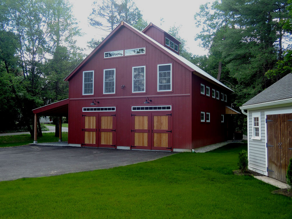 An exterior picture of the Westborough Auto Barn, designed and built by Geobarns to house a Chevrolet collection in a dream garage, with barn red wood siding, silver metal roof, hand-built barn doors, cupola, and Douglas fir trim.