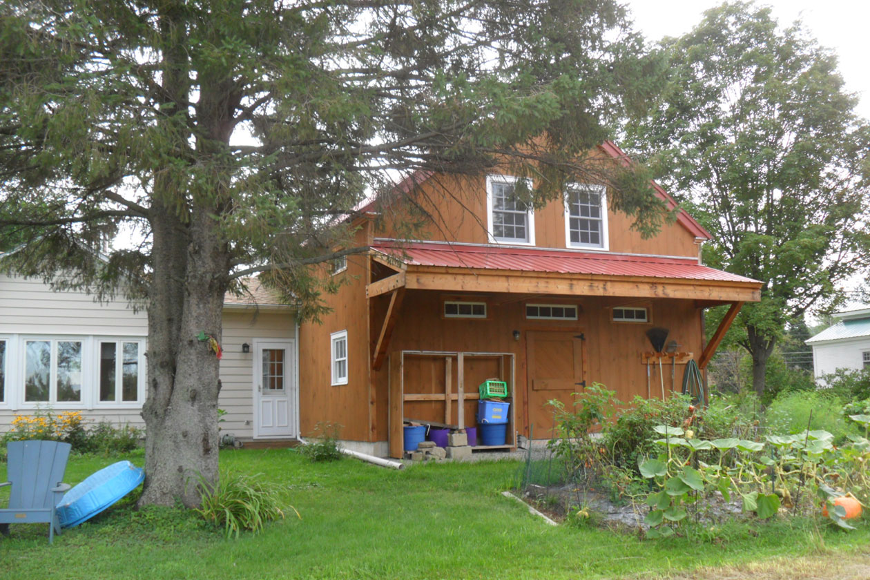 An exterior picture of the Williston Garage Barn, design and built by Geobarns, with honey-stained wood siding, brock red metal roof, cupola, and an apartment above a two-car garage.