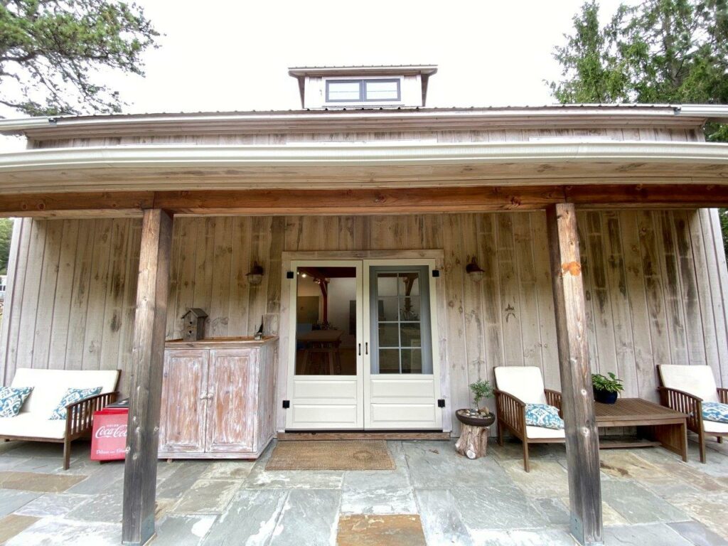 An exterior picture of the porch and entry to an art studio designed and built by Geobarns, with naturally weathered siding and a cupola.