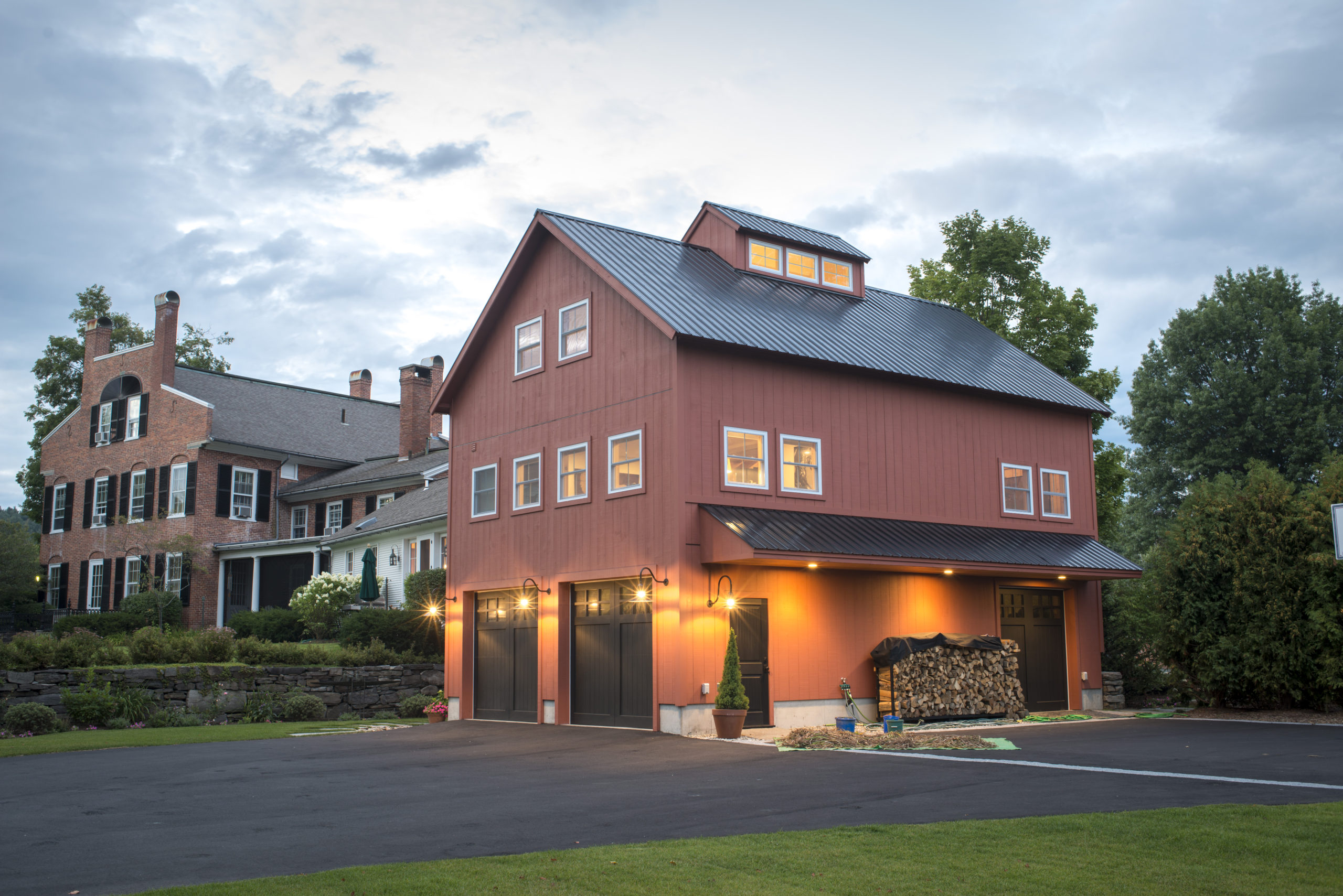 Historic Carriage House addition designed and built by Geobarns in an historic district, with barn red wood siding, black metal roof, and space for garage, recreation, and home office.