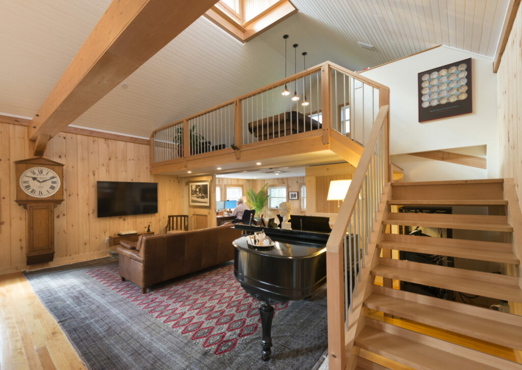 An interior picture of the Historic Carriage House, designed and built by Geobarns, showing the recreation room, sweeping staircase to the loft, pickled bead board ceiling, and exposed framing.