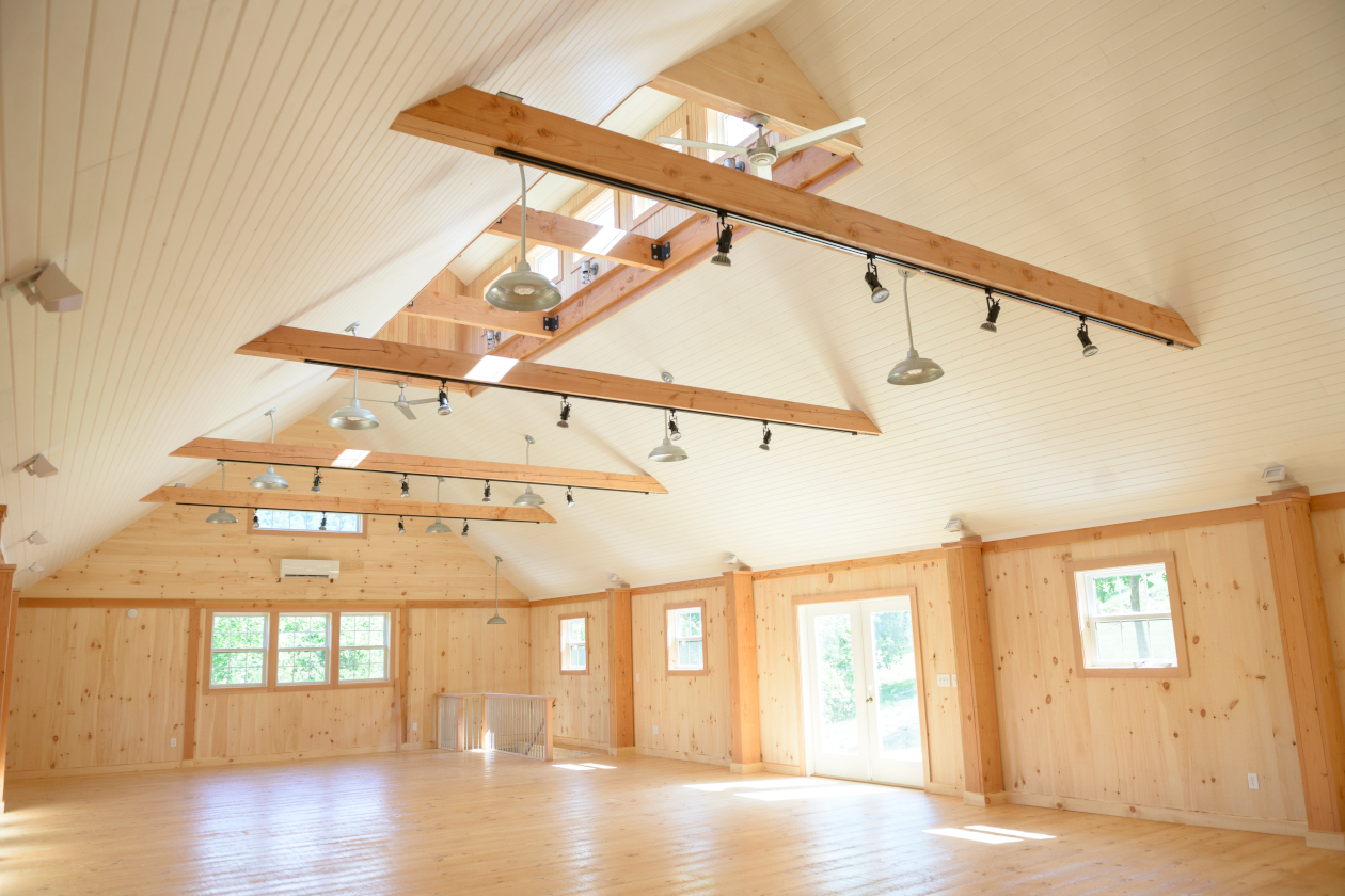 Interior picture of a furnituremaker's gallery, design and built by Geobarns, with wood paneled walls, bead-board ceiling, exposed timbers, and cupola above the vaulted ceiling.