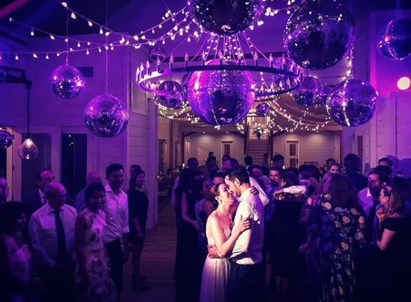 A picture of a wedding dance at the Barn at Smuggler's Notch, designed and built by Geobarns, with Christmas lights and disco balls with a crowd watching the Bride and Groom first dance, with decor by Monica Flynn