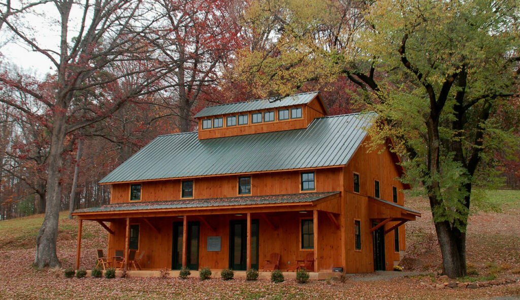 A picture of the Baldwin Center at Bundoran Farm, designed and built by Geobarns, with cherry stained wood siding, gray metal roof, and long monitor cupola. 