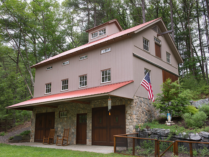 An exterior picture of the Classic Car and Family Recreation Barn, designed and built by Geobarns, with mocha wood siding, copper metal roof, hand-built garage doors, and cupola.