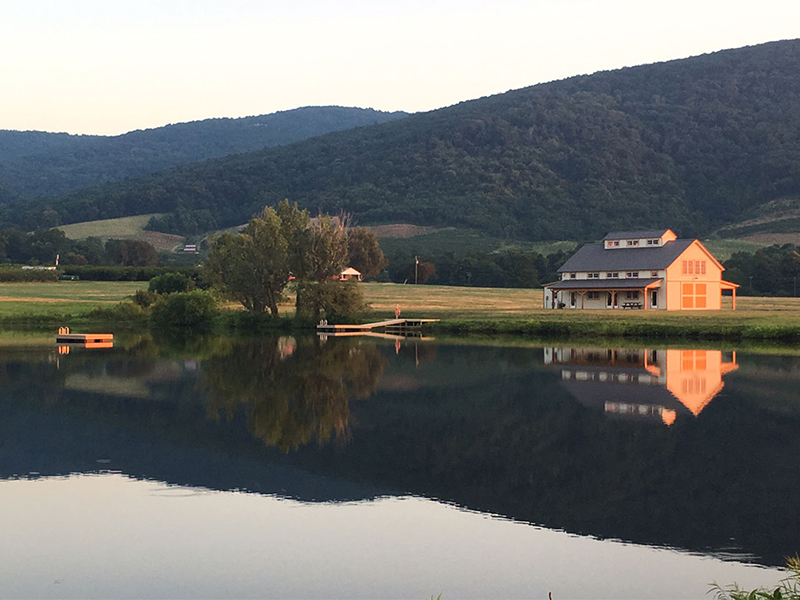 A picture of the Farm Church Barn beside a calm lake in the mountains of Virginia, designed and built by Geobarns.