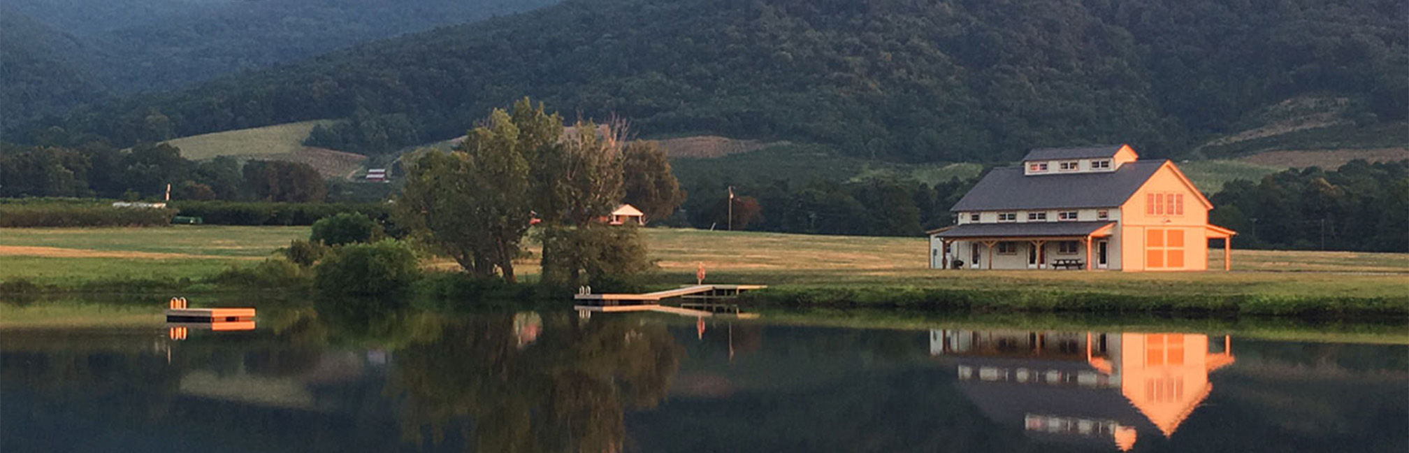 A picture of the Farm Church Barn beside a calm lake in the mountains of Virginia, designed and built by Geobarns.