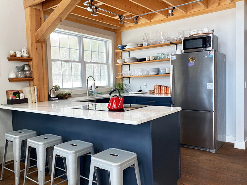 A picture of the kitchen in the Farmhouse, designed and built by Geobarns, featuring exposed ceiling rafters, exposed framing timbers, and blue cabinetry.