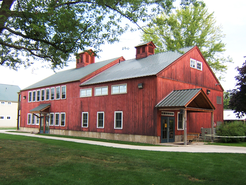 An exterior picture of the Four Rivers Charter School classroom building, design and built by Geobarns, with weathered wood siding in barn red, gray metal roof, and cupolas.
