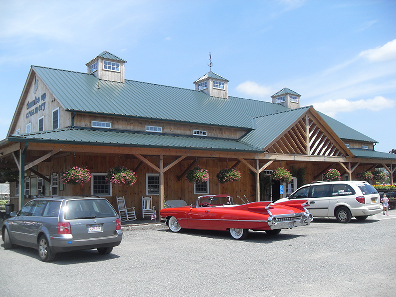 An exterior picture of the Green Thumb Nursery retail building, designed and built by Geobarns, with green metal roof and weathered wood siding, with multiple cupolas and a wrap-around porch.
