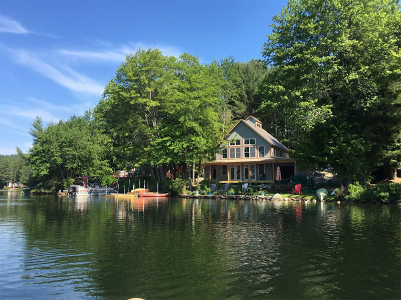An exterior picture of the Lake House and Barn, designed and built by Geobarns, on the forested shore of a lake in New England.
