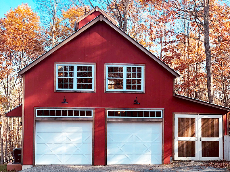 A picture of the Geobarns Office Barn, designed and built by Geobarns, with barn red wood siding, silver metal roof, two car garage, and a side shed with hand-built swing doors.