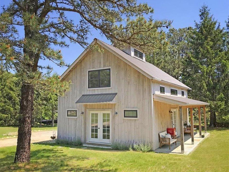 An exterior picture of an art studio, designed and built by Geobarns, with naturally weathered wood siding, burnished bronze metal roof, front porch, and cupola.