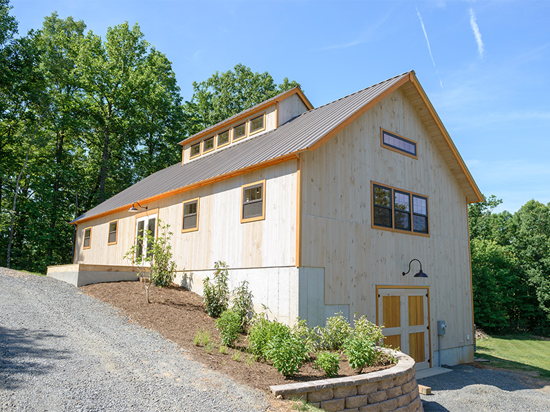 An exterior picture of a artisan woodworking studio, designed and built by Geobarns, with natural colored wood siding, Douglas fir trim, burnished bronze metal roof, and a long monitor cupola. 