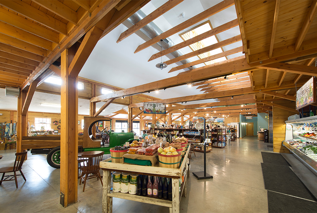 The interior of Waterfresh Market in Massachusetts, design and built by Geobarns, showing produce stands, exposed framing, monitor cupola, and a Ford Model T farm truck on display.