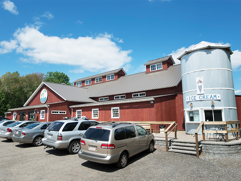 An exteriro picture of the Waterfresh Market, design and built by Geobarns, with barn red wood siding, gray metal roof, cupolas, and a silo for selling ice cream.