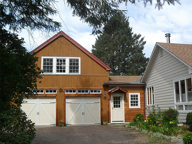 An exterior picture of the Williston Garage Barn, design and built by Geobarns, with honey-stained wood siding, brock red metal roof, cupola, and an apartment above a two-car garage.