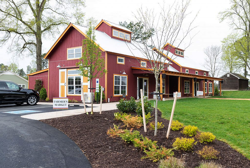 An exterior picture of the Farm at Chickahominy Falls, designed and built by Geobarns, with barn red wood siding, silver metal roof, next to the community garden.