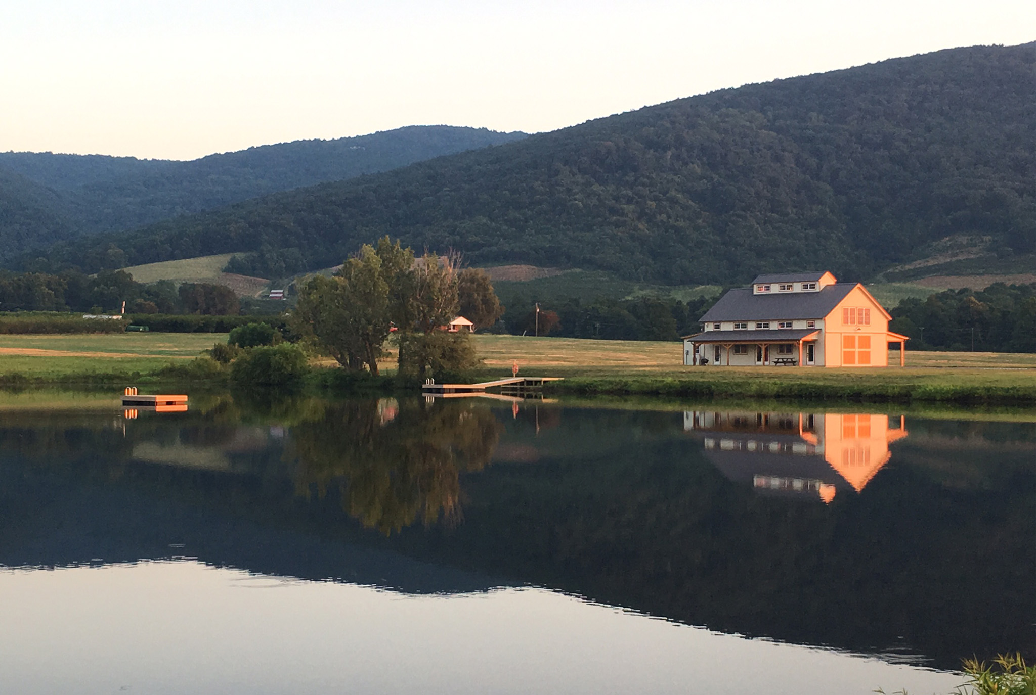 A picture of the Farm Church Barn, designed and built by Geobarns, beside a calm lake with Virginia mountains in the background.
