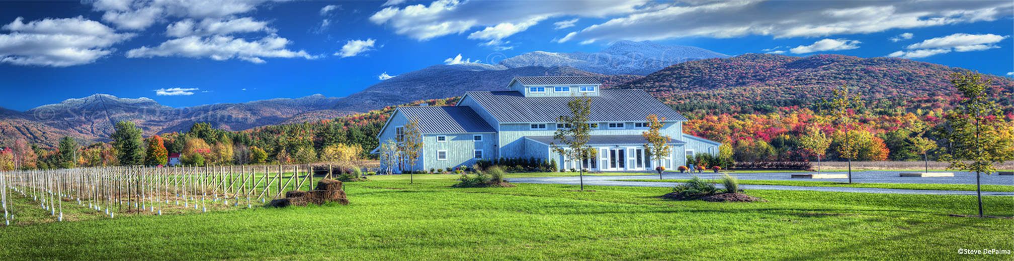 A panoramic picture of the Barn at Smuggler's Notch wedding venue with fall foliage on Mount Mansfield and Mount Stowe in the background