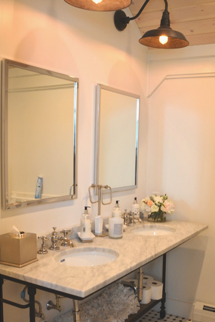 A picture of a bathroom at the Barn at Smuggler's Notch in Vermont showing chrome fixtures and mirrors, with a gooseneck barn light fixture, designed and built by Geobarns.